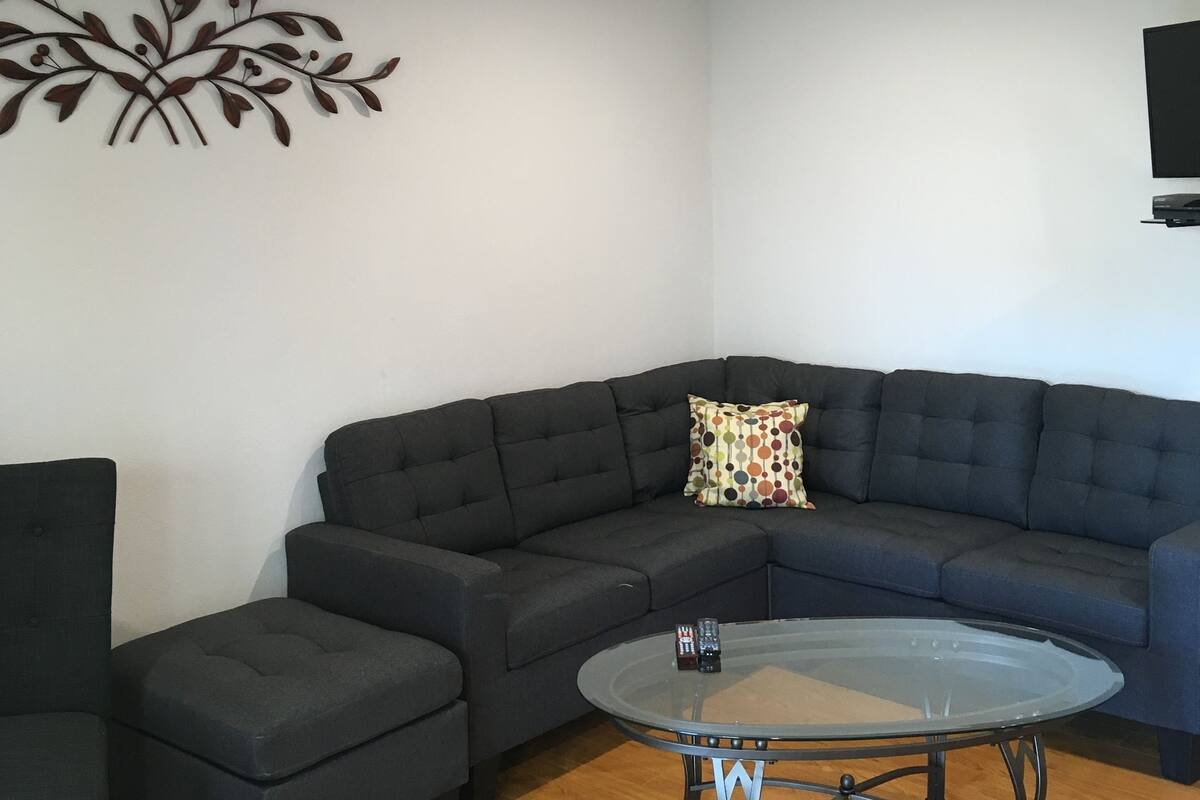 A modern living room with a sectional sofa, a glass coffee table, and a decorative wall piece.