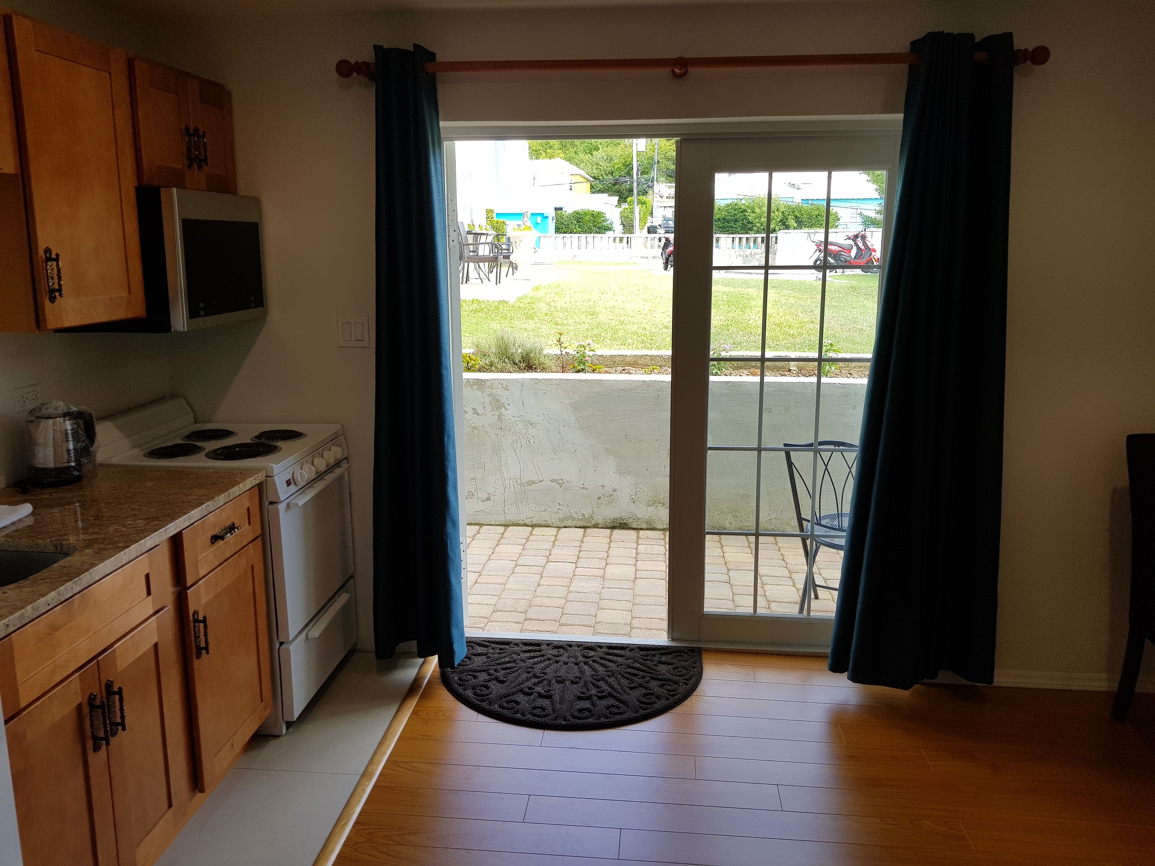 A kitchen with wooden cabinets, a stove, and a microwave. There is a sliding glass door leading to a patio with a chair and a table.