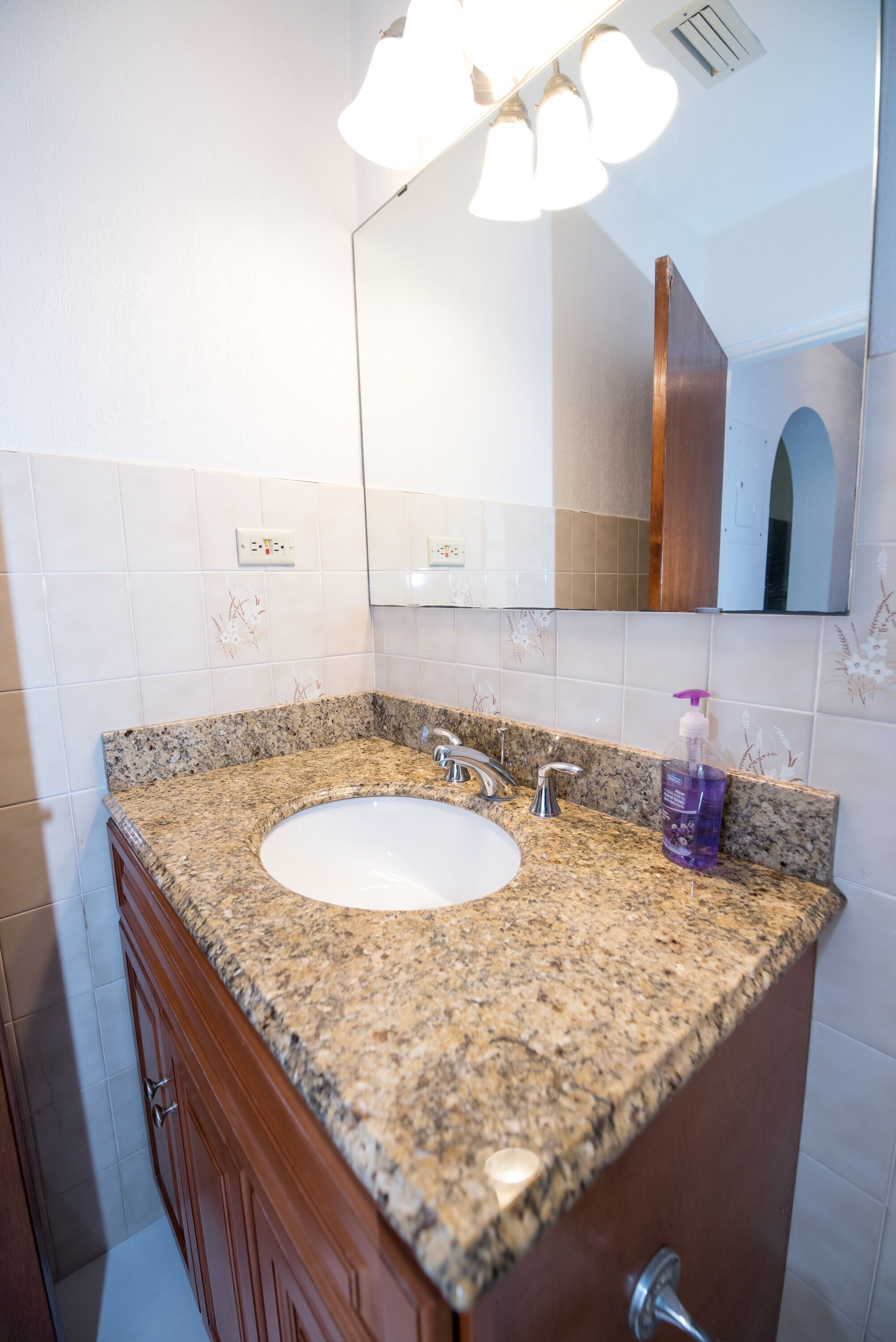 A bathroom with a granite countertop sink, a mirror, and a wooden cabinet.