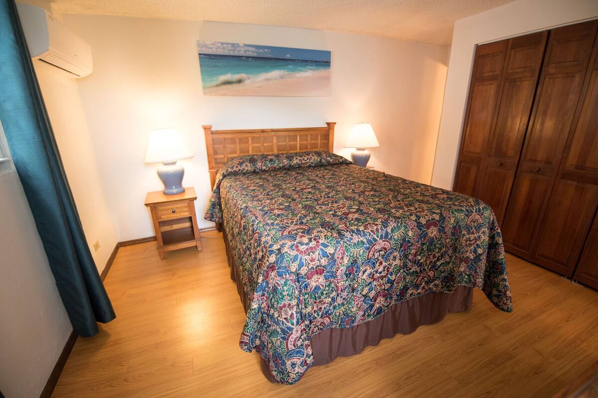 A bedroom with a wooden bed, two bedside tables with lamps, a wooden floor, a painting on the wall, and a wooden wardrobe.