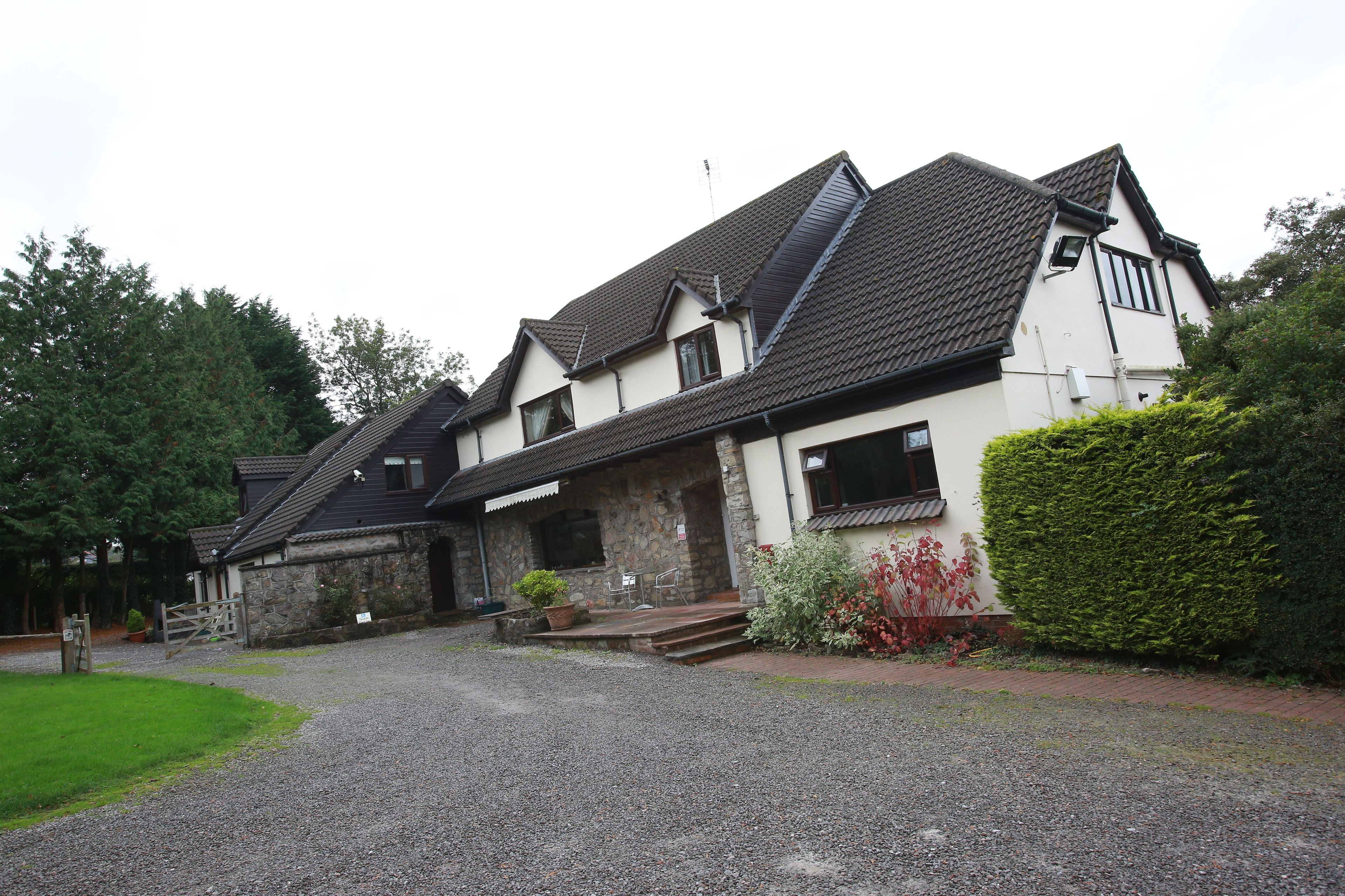 A two-story house with a stone facade, a tiled roof, and a gravel driveway leading to the entrance.