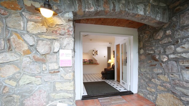 Una entrada de paredes de piedra con suelo de baldosas que conduce a una habitación con cama y lámpara.