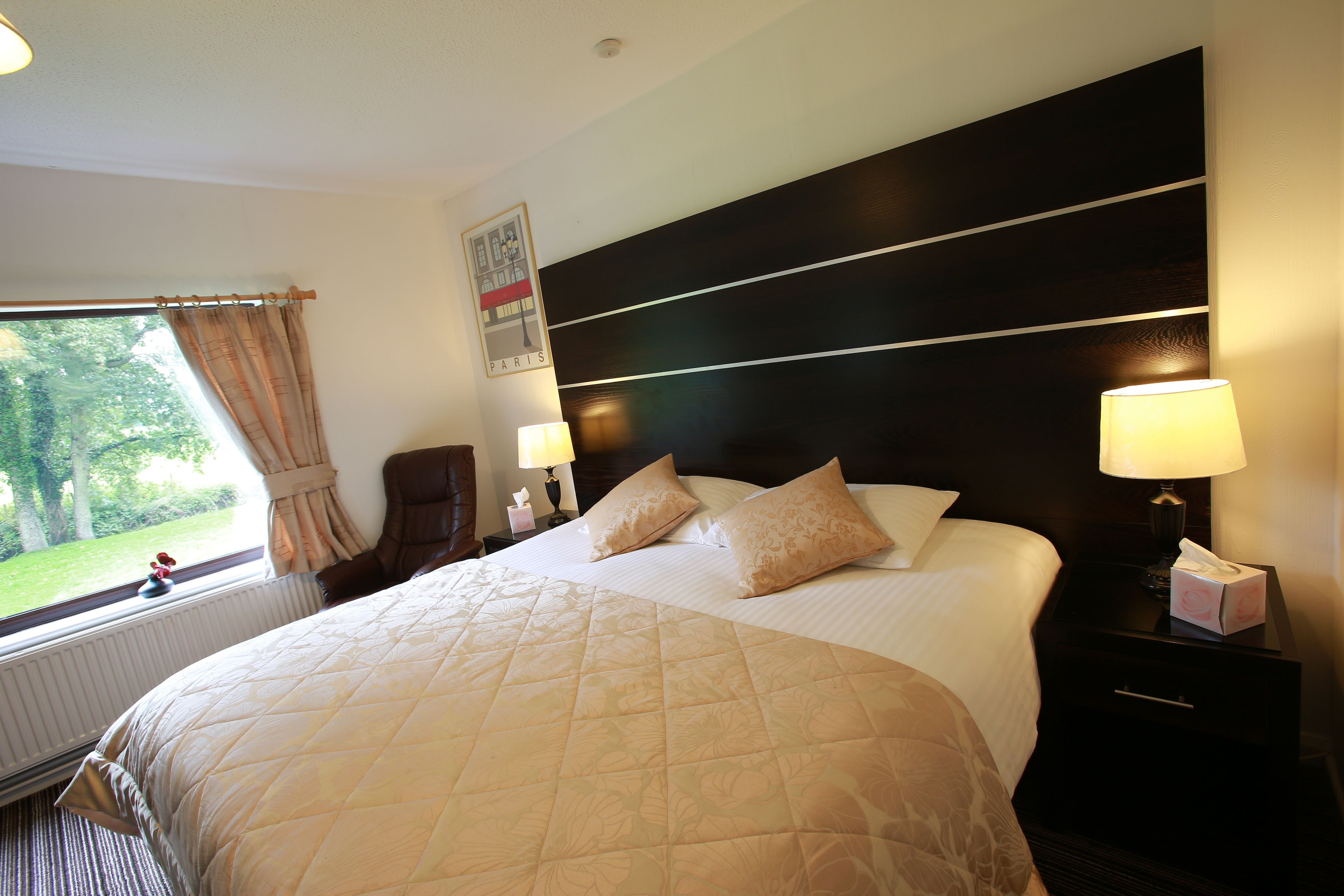 Een hotelkamer met een groot bed, twee bedlampjes, een nachtkastje, een stoel en een raam met gordijnen.
