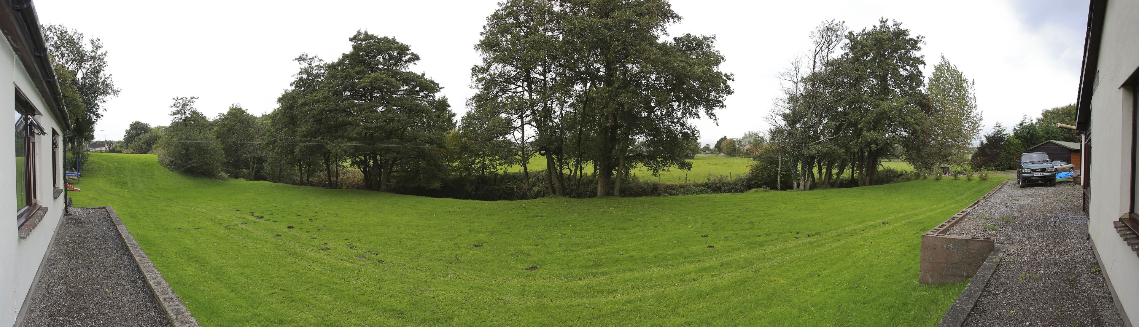Un campo cubierto de hierba con árboles y un edificio al fondo.