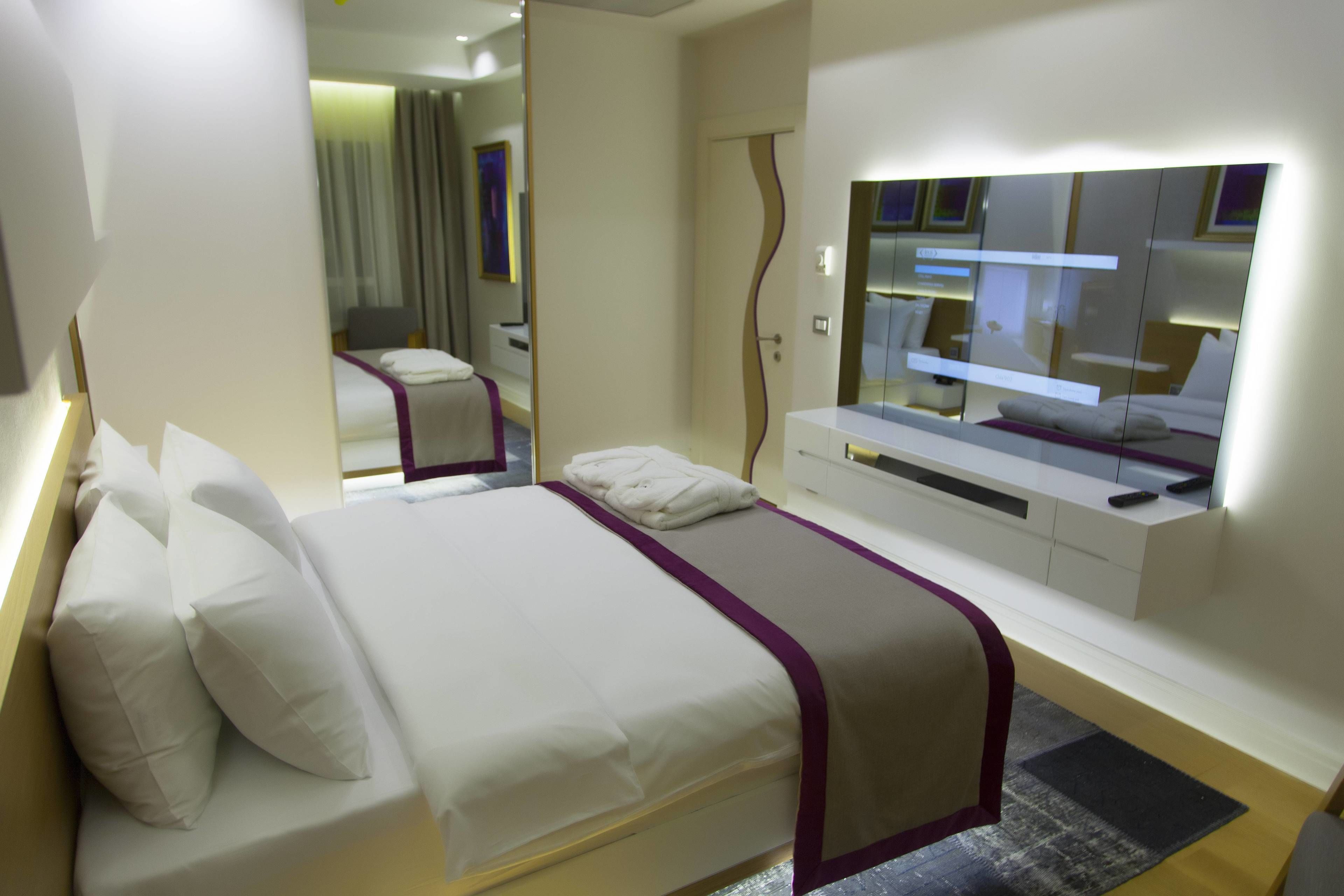 A modern hotel room with a large bed, a TV, and a mirror.