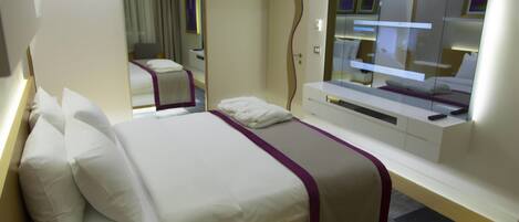 A modern hotel room with a large bed, a TV, and a mirror.