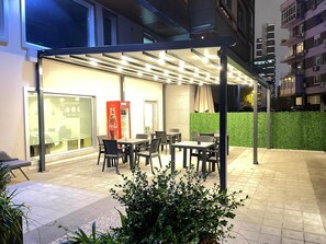 An outdoor seating area with tables and chairs, a Coca-Cola vending machine, and a green hedge. - The Leos Residence (Istanbul)