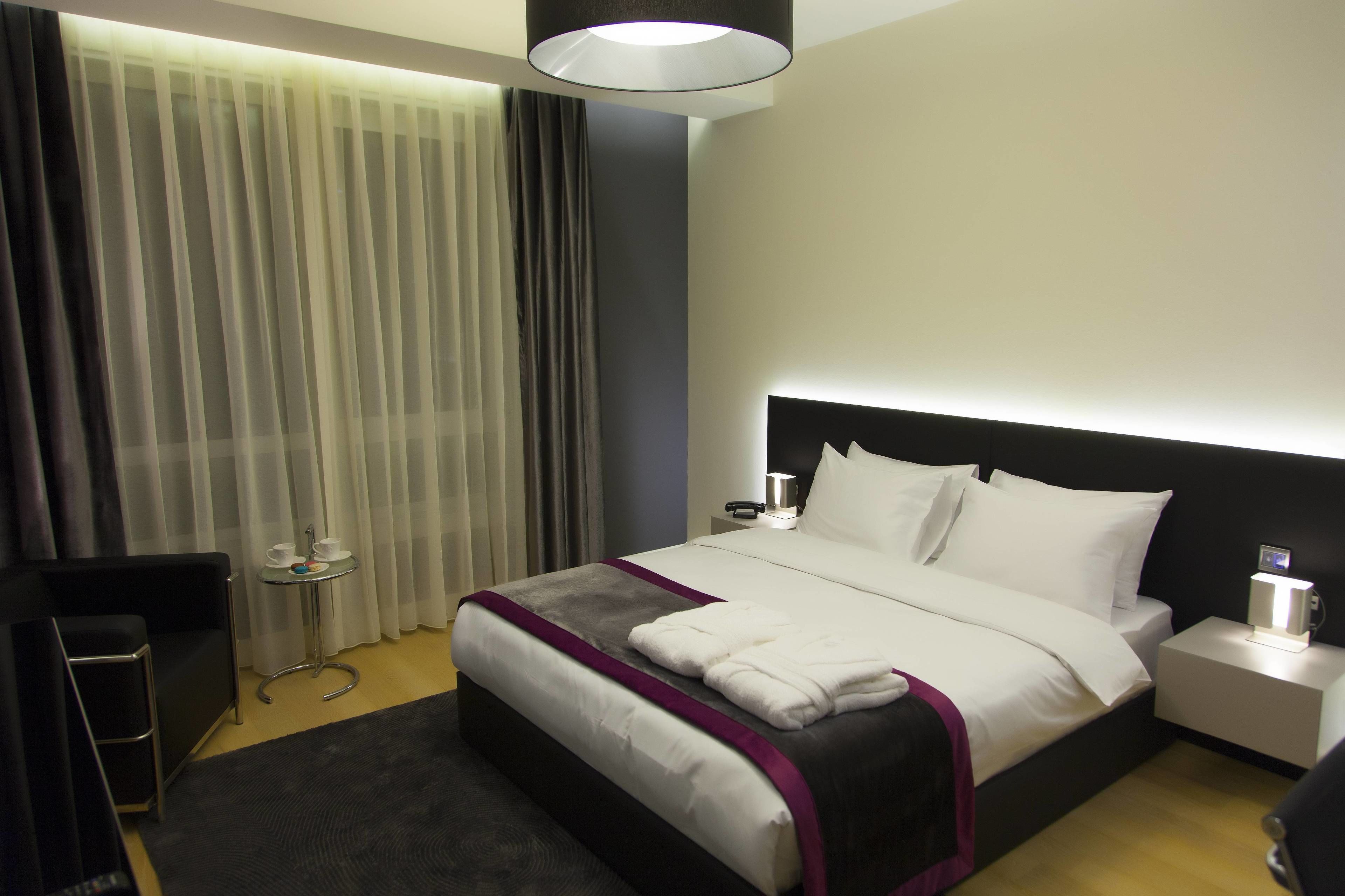 Una habitación de hotel con cama, mesita de noche, lámpara y una pequeña mesa con tazas y bandeja.