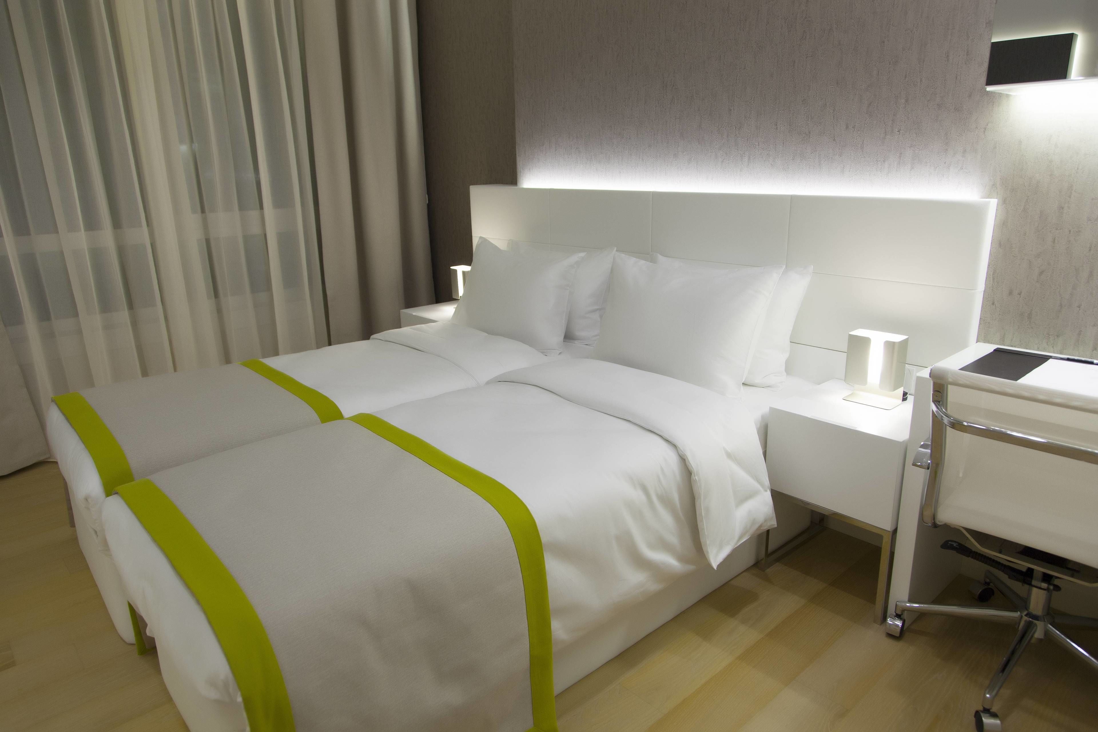 Una camera d'albergo con un letto rifatto, un comodino con una lampada e un piccolo carrello.