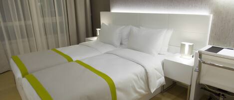 Una camera d'albergo con un letto rifatto, un comodino con una lampada e un piccolo carrello.