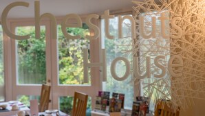 A room with a large window, a wooden chair, and a table with various items. - Chestnuts House (Bath)