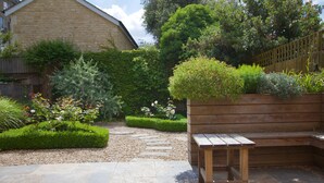 A stone patio with a wooden bench and a garden area with various plants and a wooden fence. - Chestnuts House (Bath)