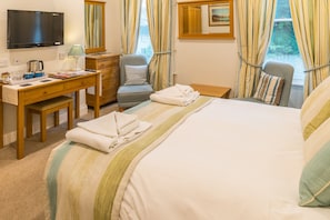A hotel room with a bed, a desk, a chair, a television, and a window with curtains.