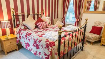Un dormitorio con cama, mesita de noche, silla y cortinas.