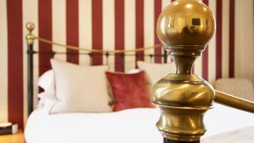 Una cama con almohadas blancas y rojas, un cabecero de bronce y una pared a rayas al fondo.
