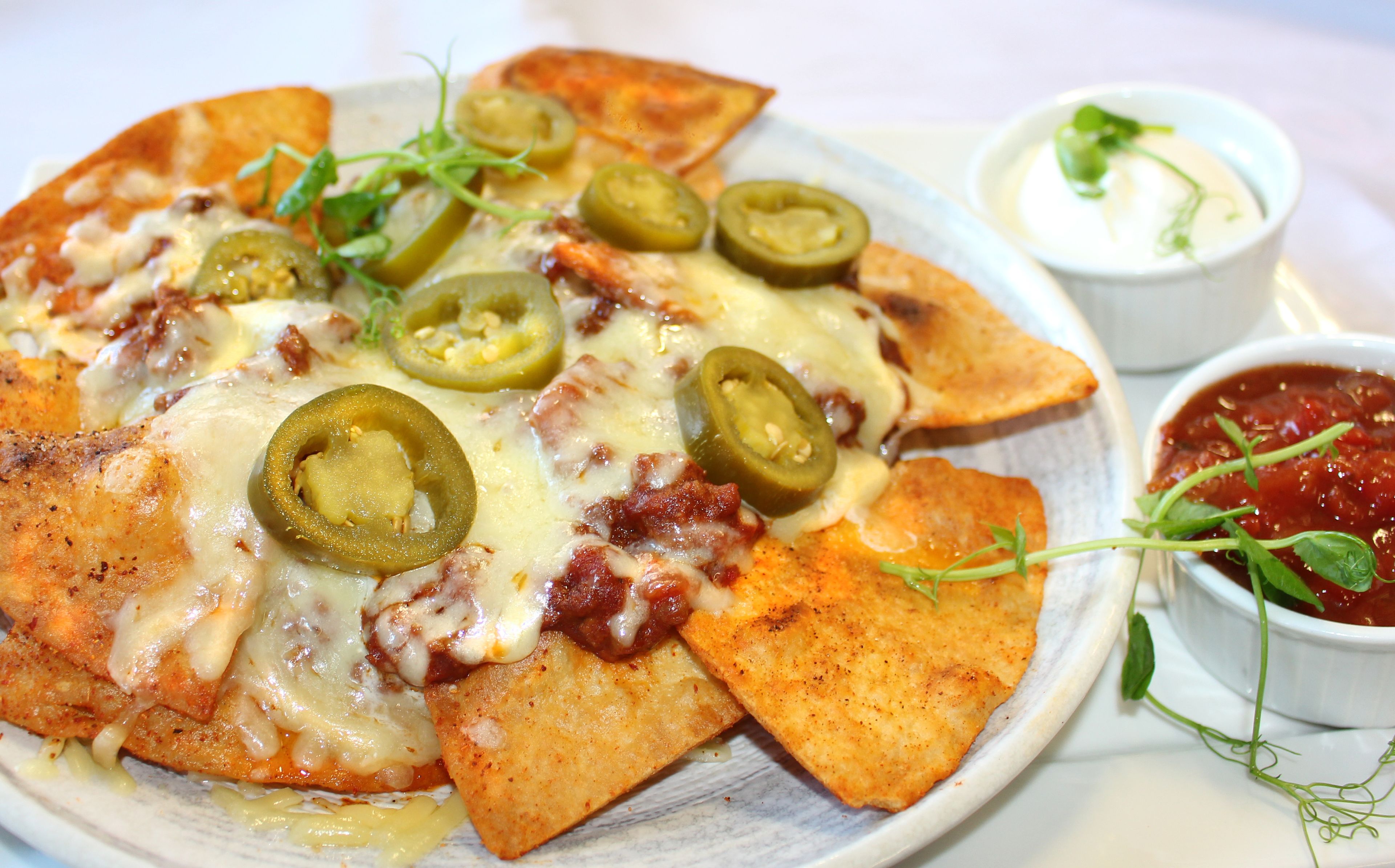 Een bord nachos met gesmolten kaas, jalapeños en een portie zure room en salsa.