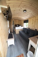 Interior de cabaña compacto con cama, sofá y pequeña mesa de comedor.