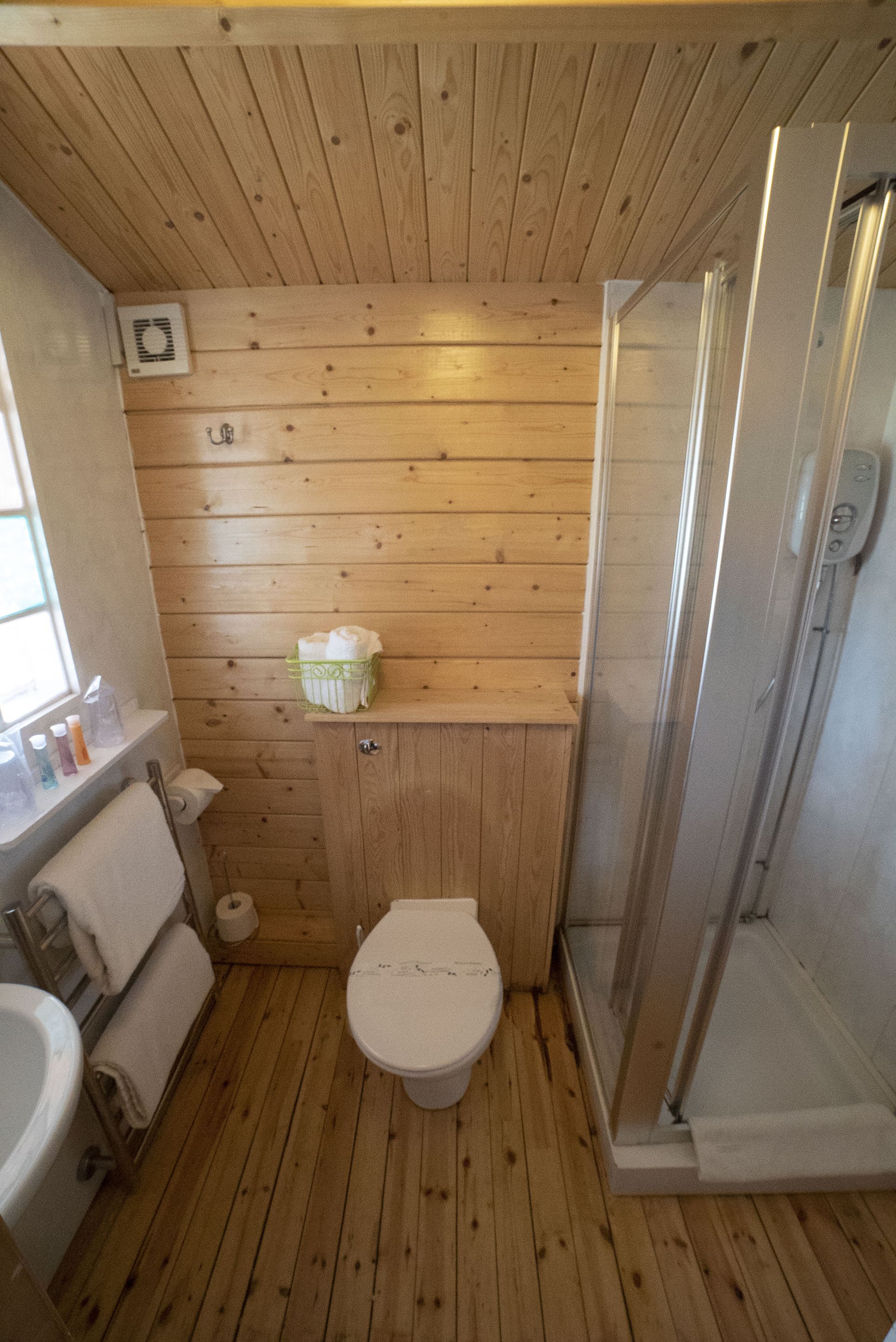 A small wooden bathroom with a toilet, sink, and shower.