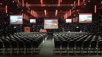 An auditorium with rows of chairs, a stage, and multiple screens displaying images.