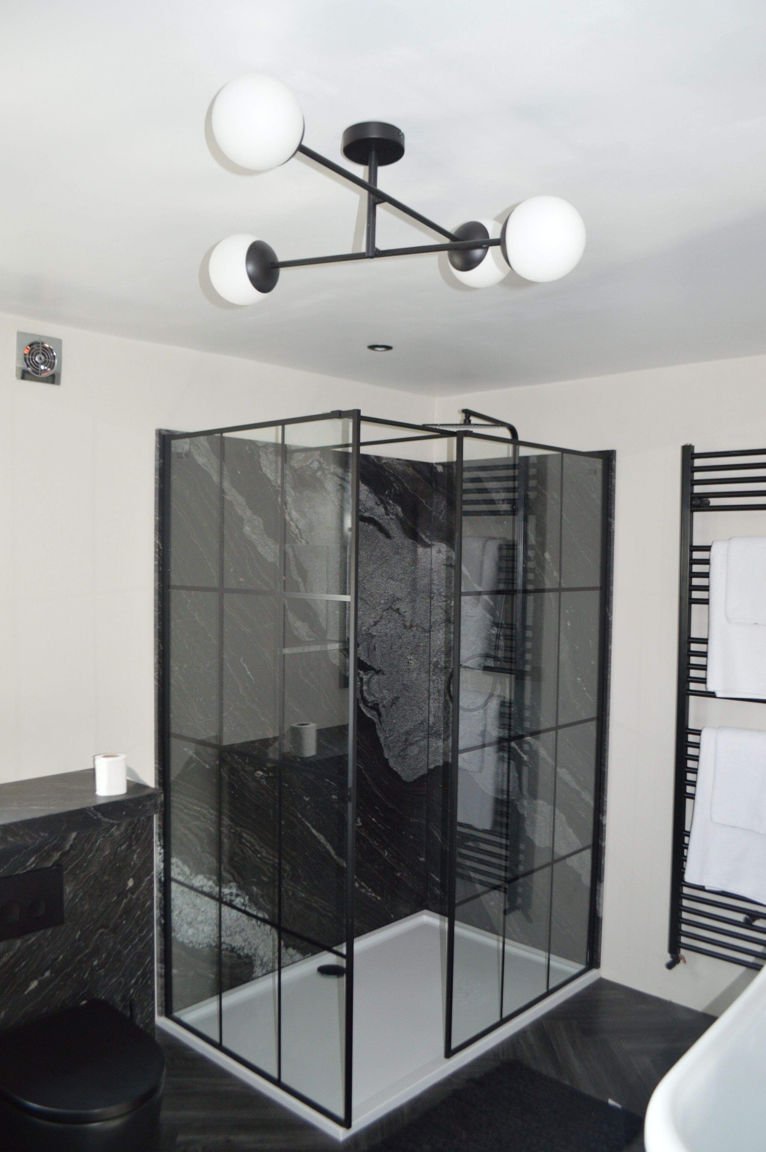 A modern bathroom with a glass-enclosed shower, a black marble countertop, and a black towel rack.