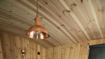 Une pièce de cabane en bois comprenant un lit, un luminaire suspendu et une fenêtre avec un store.