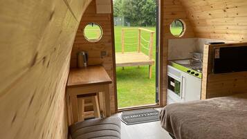A cozy cabin with a wooden interior, a small kitchenette, a bench, and a view of a grassy yard.