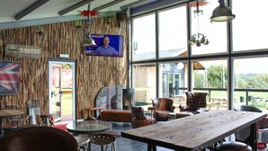 Un interior rústico con una pared de madera, una gran mesa de madera, sillas de cuero y una pantalla de televisión.