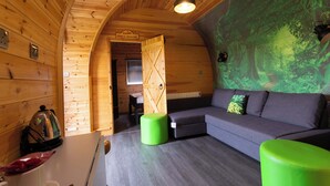 Un interior de cabaña acogedor con paredes de madera, un sofá gris, otomanas verdes y una mesa de centro.