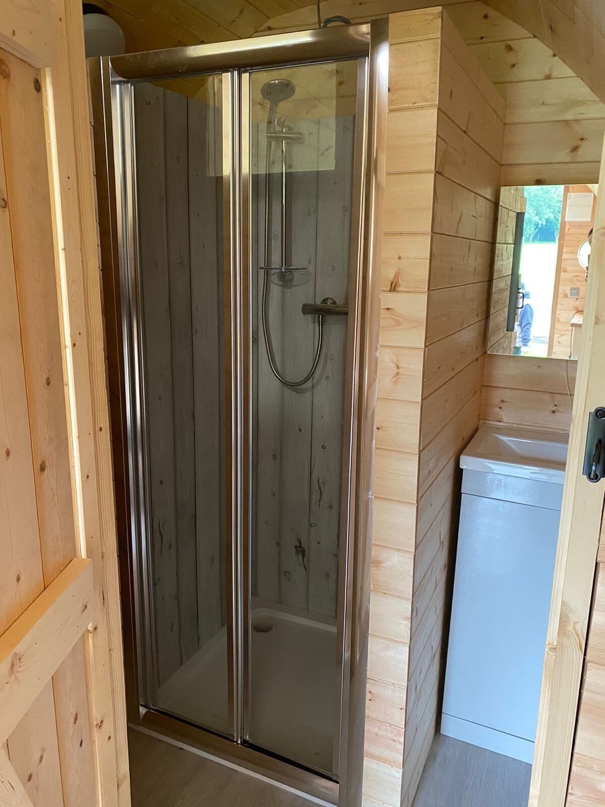 A wooden cabin with a glass-enclosed shower stall, a sink, and a mirror.