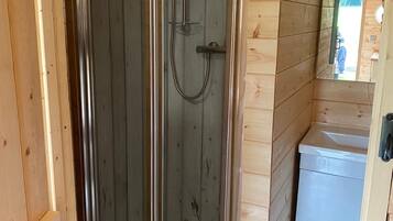 A wooden cabin with a glass-enclosed shower stall, a sink, and a mirror.