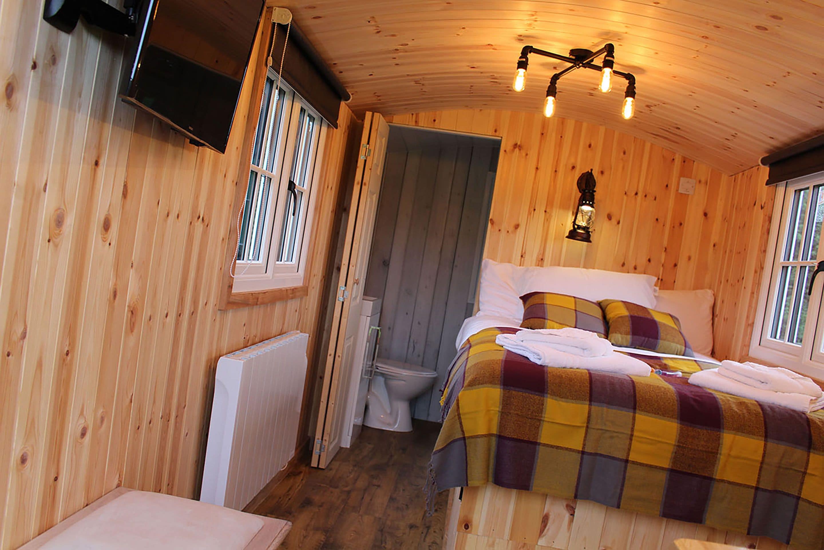 Una habitación de cabaña de madera con una cama, una ventana, un radiador y un inodoro.