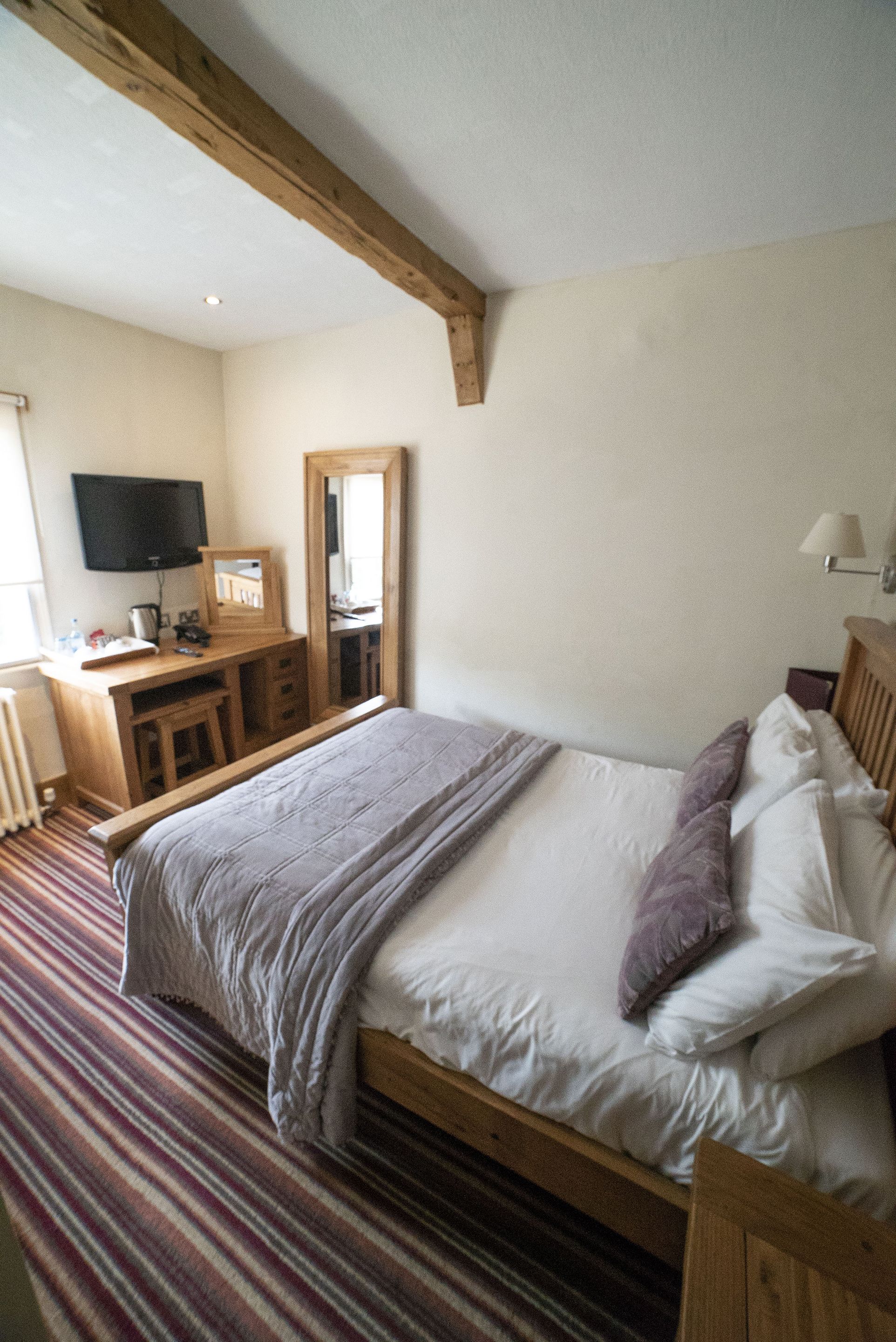 A bedroom with a wooden bed, a desk with a mirror, a television, and a lamp.