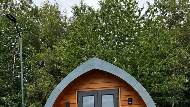 Una cabaña pequeña de madera con un letrero que dice “SALLY” y una terraza con sillas.