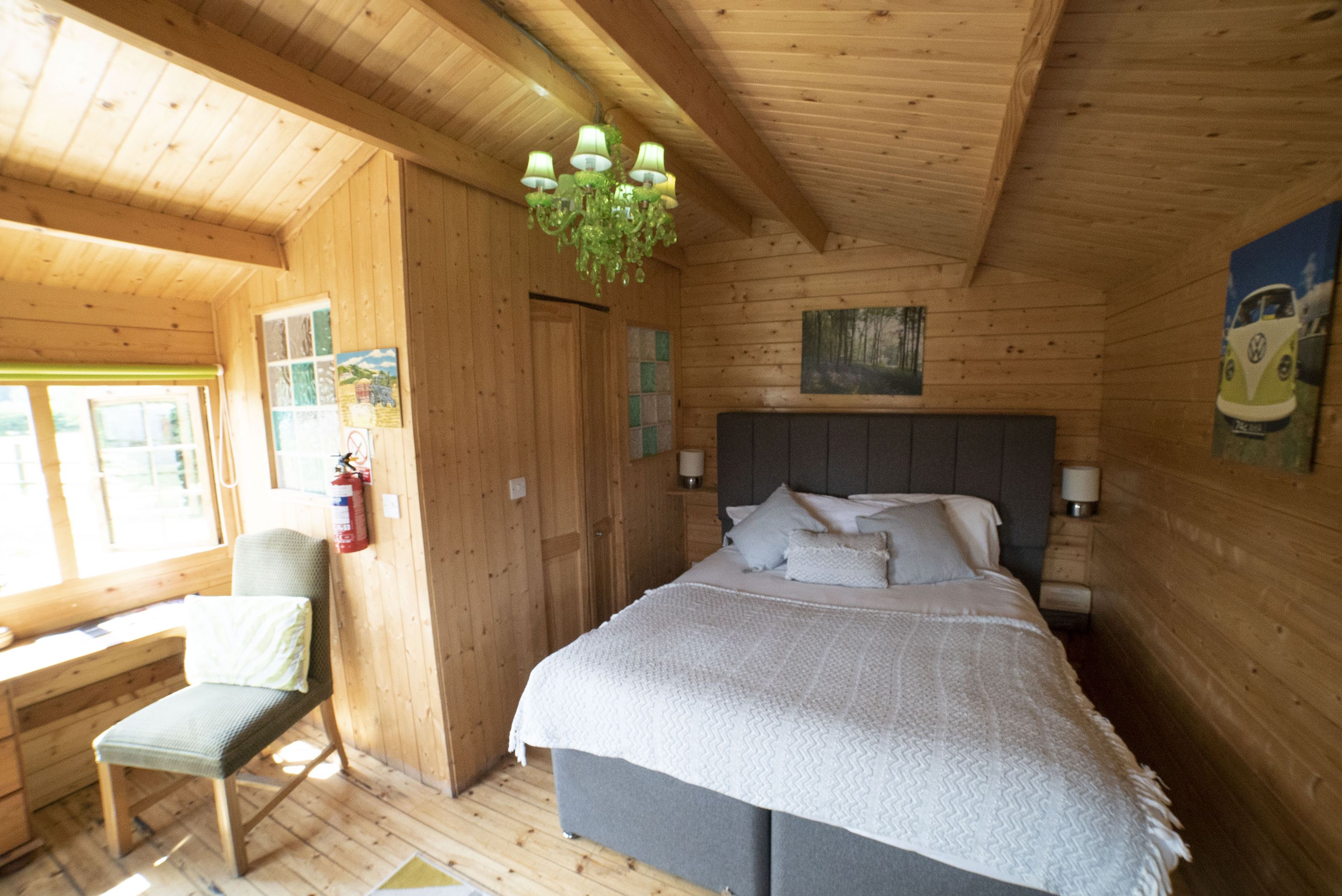 Camera da letto in una baita di legno, con un letto, una sedia, una scrivania e un lampadario.