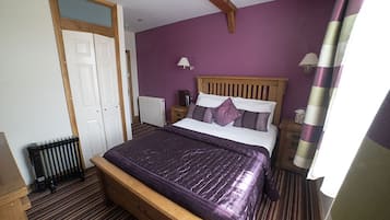 A bedroom with a wooden bed, purple bedding, a white radiator, and a wooden floor.