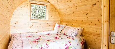A wooden cabin bedroom with a bed, a window, and a door.