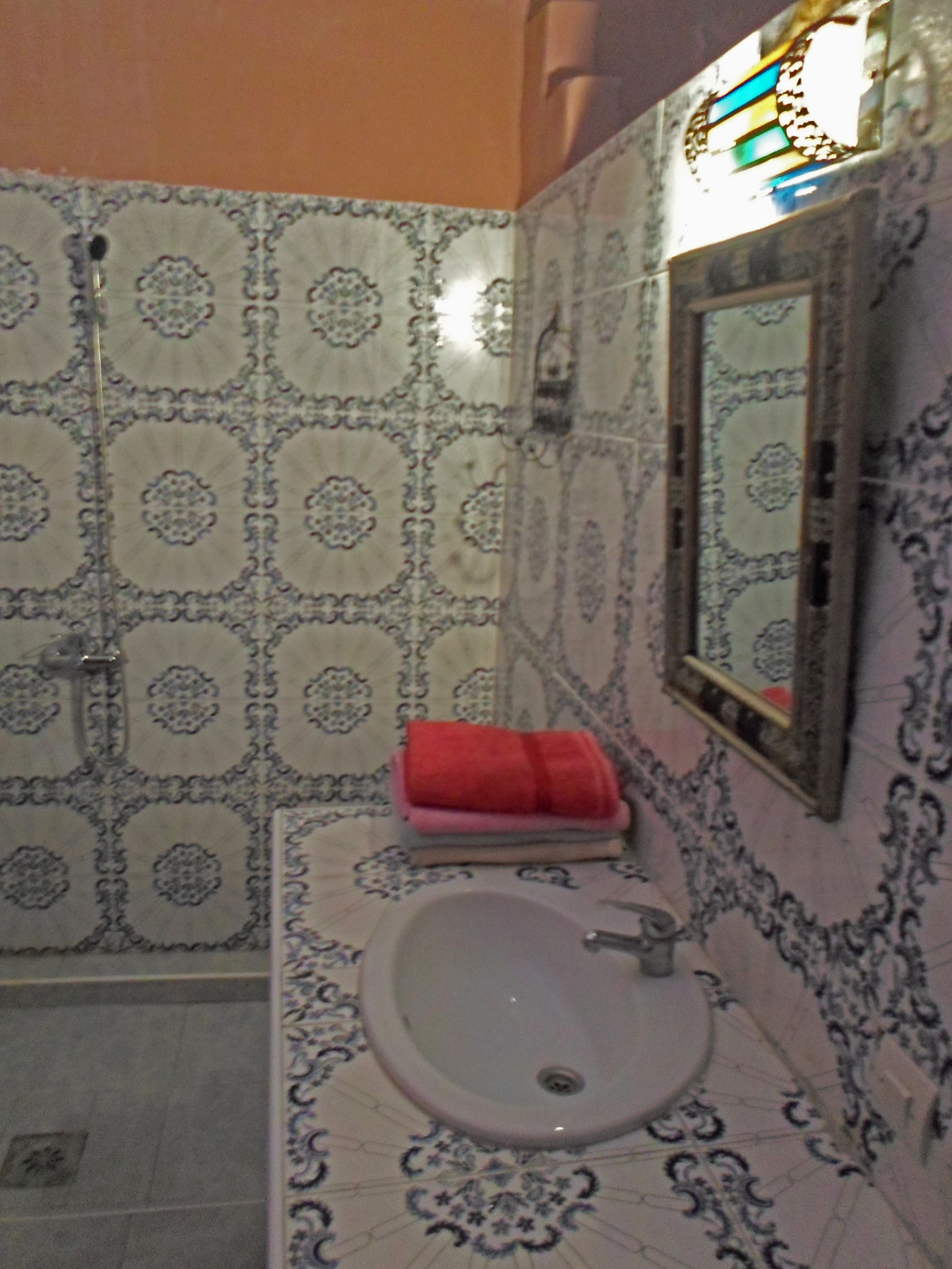 A bathroom with patterned tiles, a sink, a mirror, and a red towel.