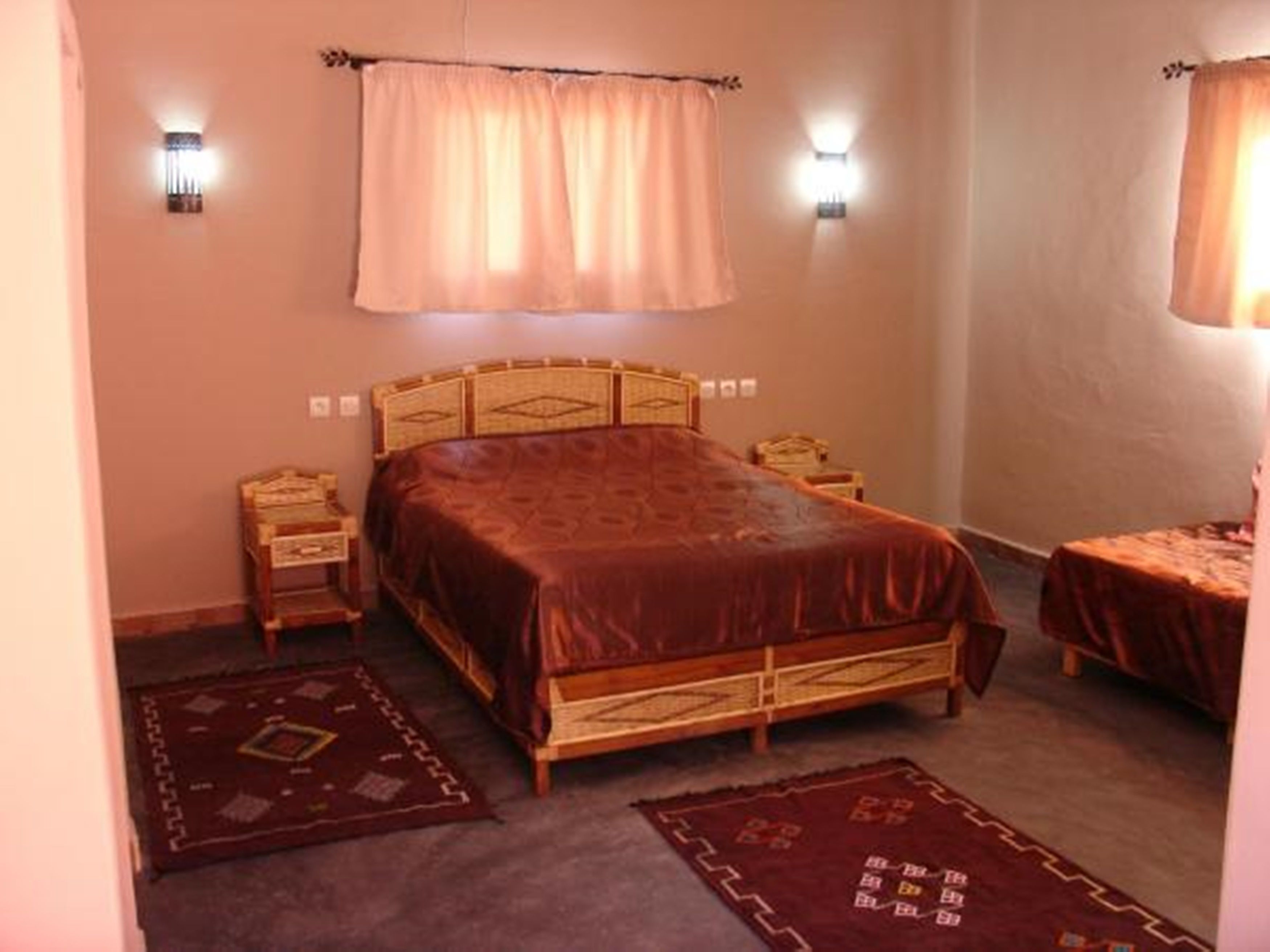 Een slaapkamer met een houten bed, twee nachtkastjes, een raam met gordijnen en twee wandlampen.