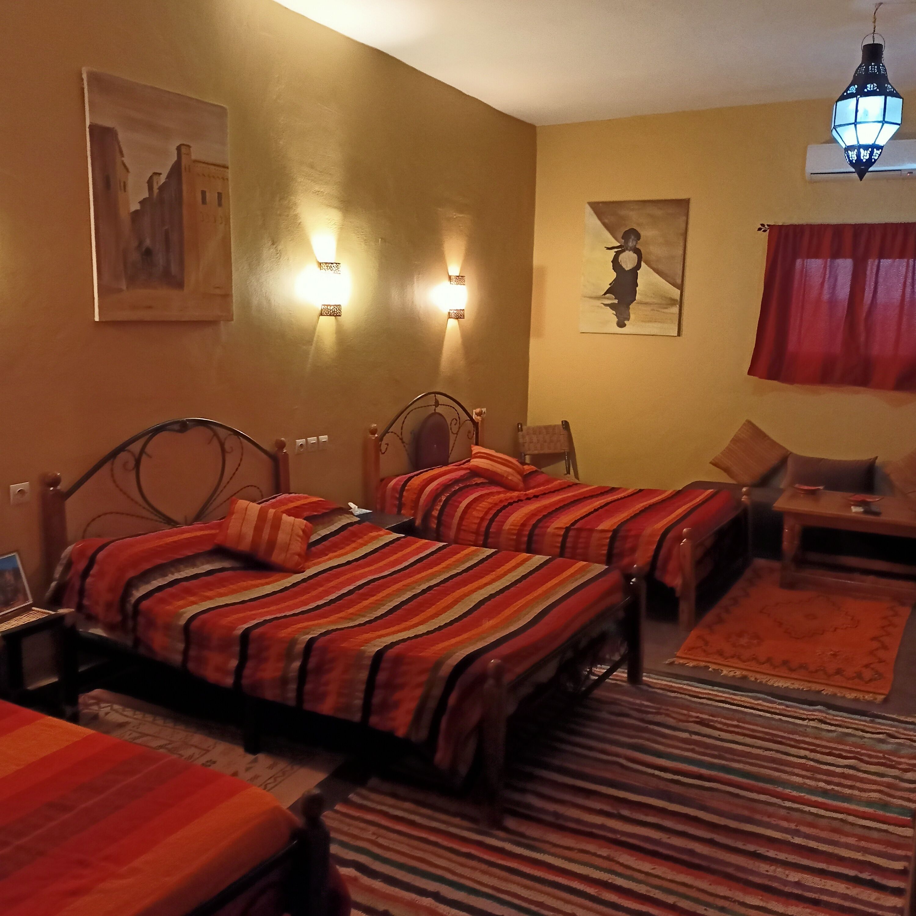 A hotel room with two beds, a desk, a chair, a lamp, and artwork on the walls.