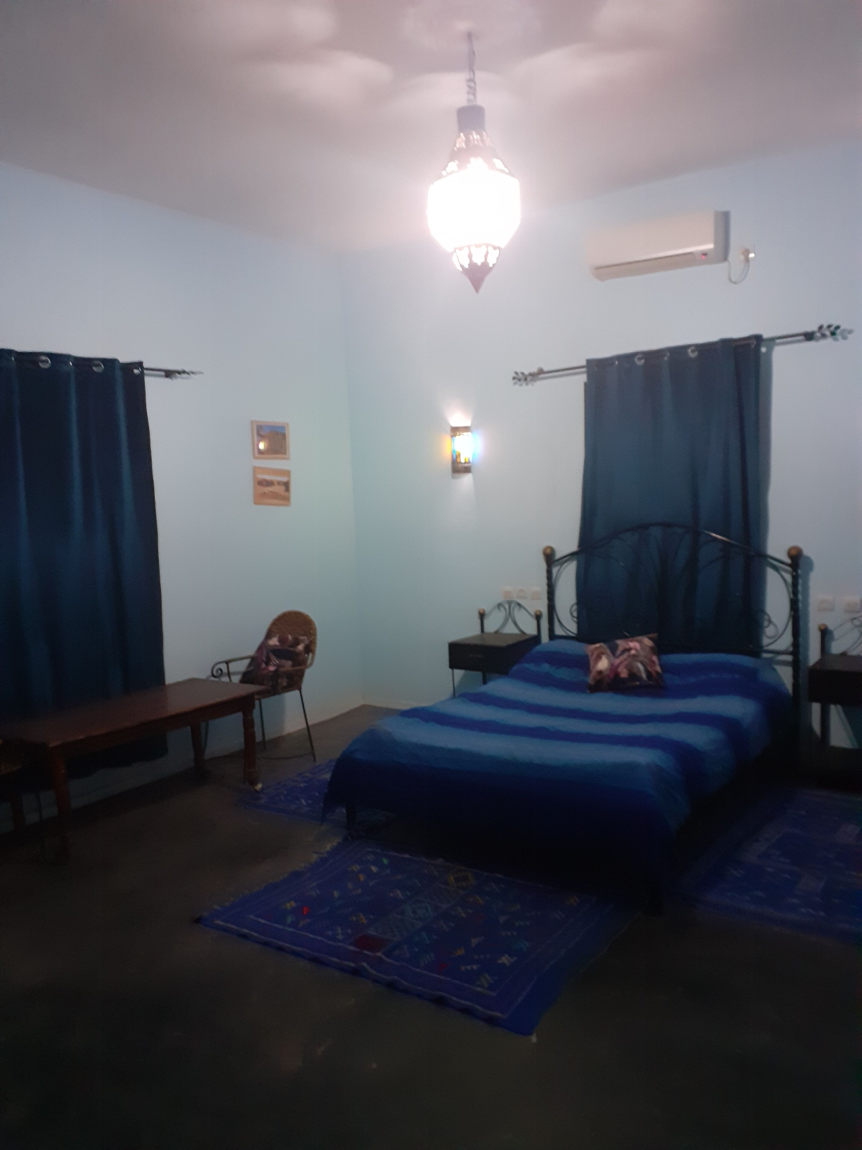 Een slaapkamer met een bed, een stoel, een bureau en een hanglamp.