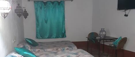 A room with a bed, a table, chairs, a TV, and a hanging light fixture.
