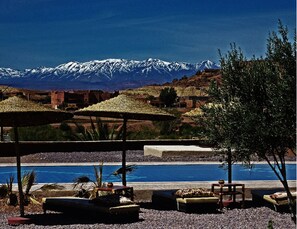 Un área de piscina con sillones de descanso y sombrillas, un paisaje montañoso y un terreno desértico.
