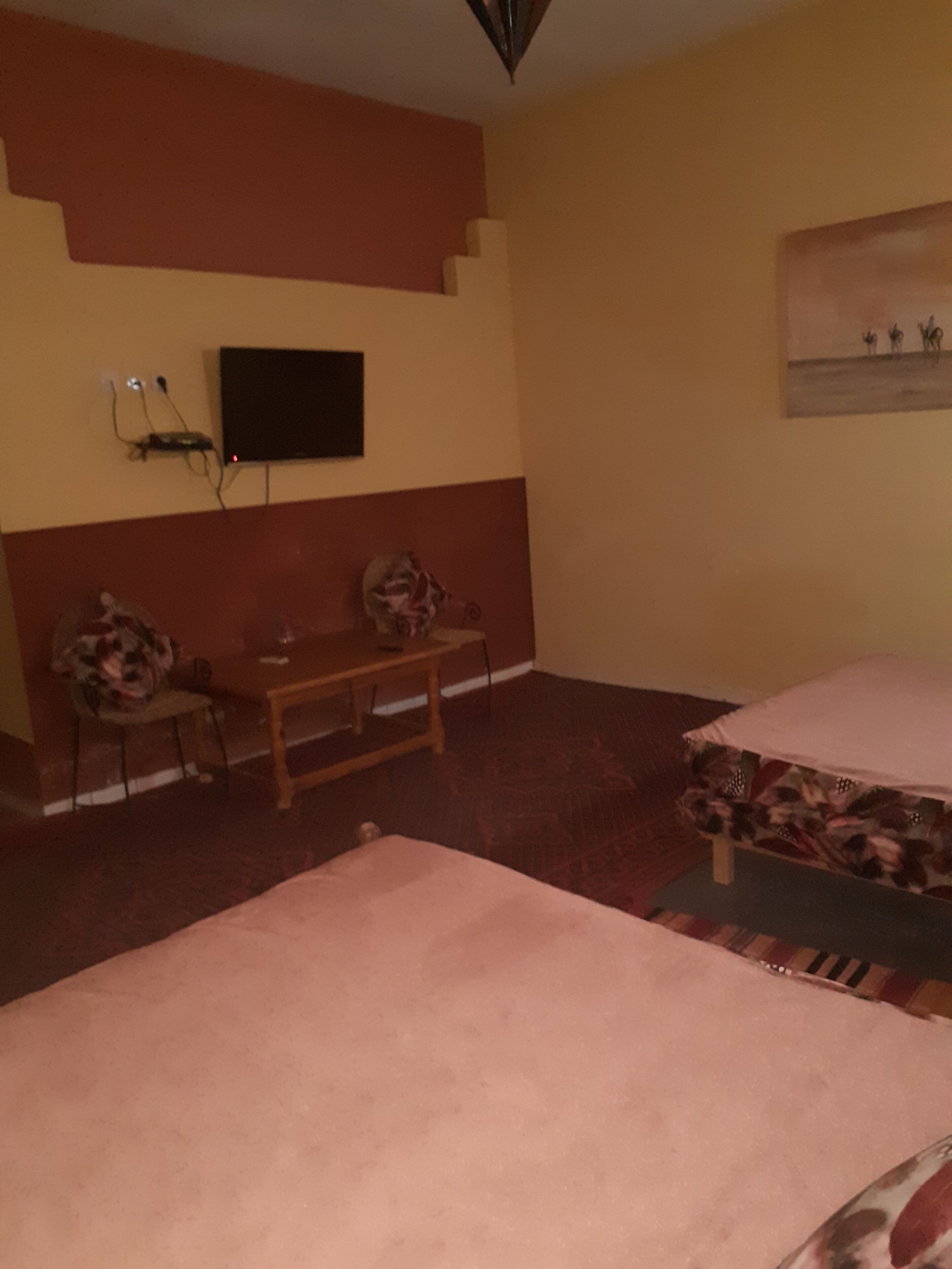 Una habitación con una cama, un escritorio, una silla, un televisor montado en la pared y un cuadro en la pared.
