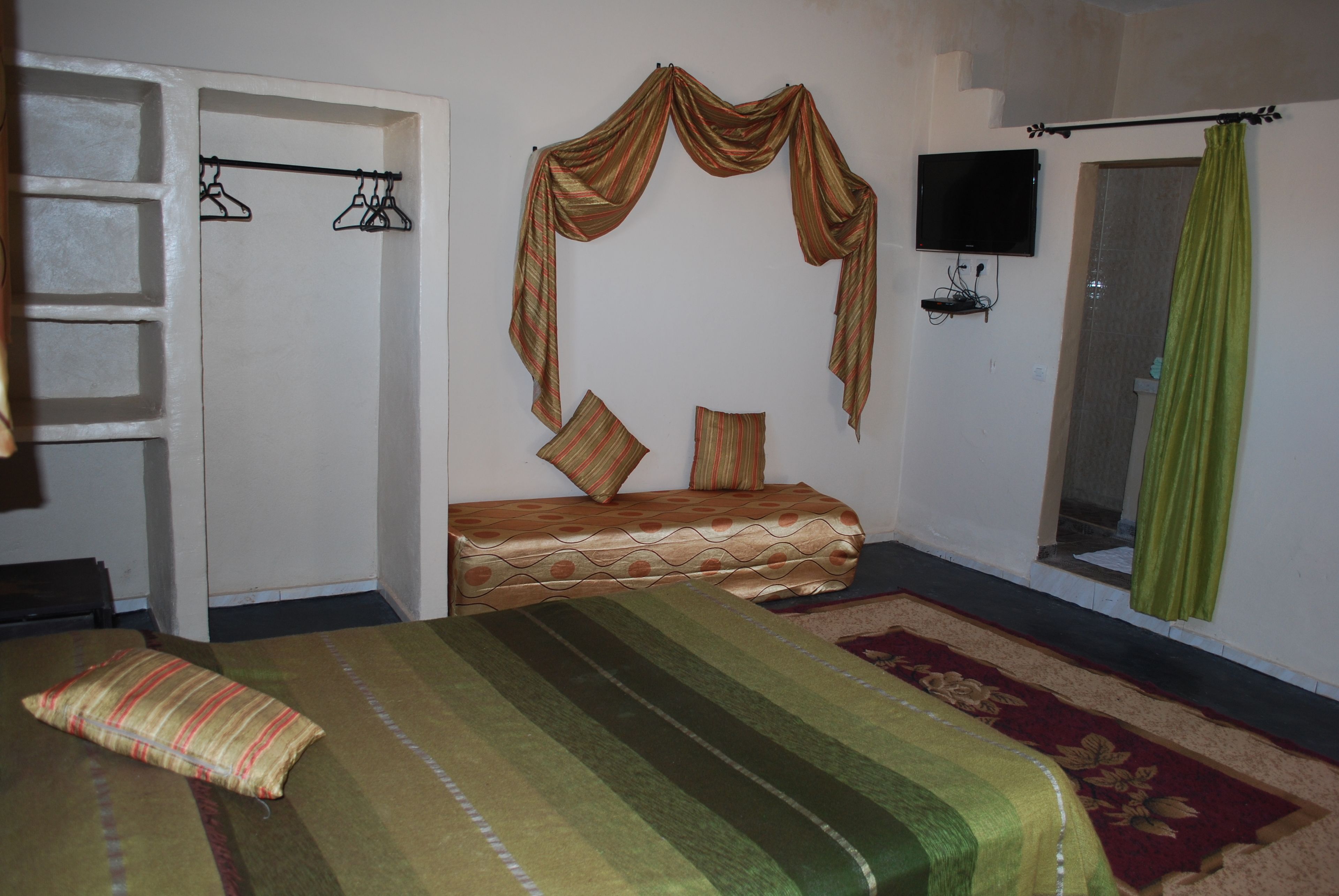 A bedroom with a bed, a wardrobe, a TV, and a green curtain.
