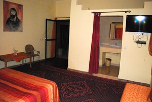 A hotel room with a bed, a chair, a television, a bathroom with a mirror, and a red curtain.