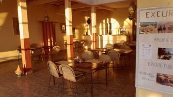 A dining area with tables and chairs, a bulletin board with excursion information, and a tiled floor.