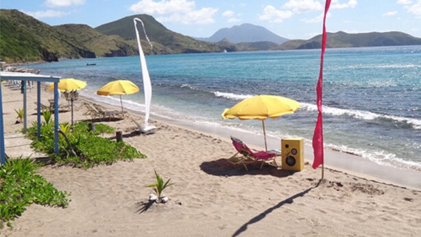 A beach with yellow umbrellas, a red flag, and a speaker on the sand.