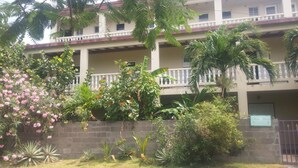 A multi-story building with balconies, surrounded by various plants and shrubs.