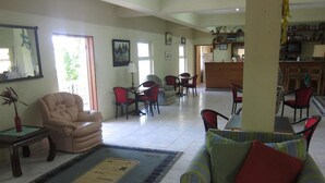 A spacious living area with a sofa, chairs, and a dining table. There is a kitchen area in the background with a counter and chairs.