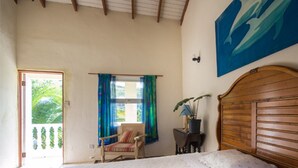 A bedroom with a bed, a chair, a window with curtains, a plant, and a painting on the wall.
